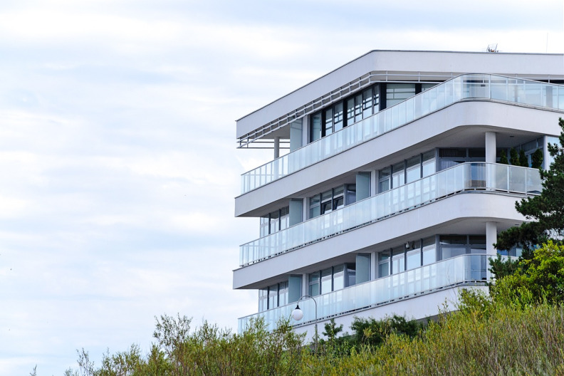 Image of a three story apartment building with glass railings and  cloudy background